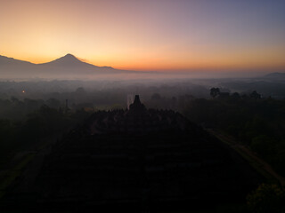 Aerial view of a temple at sunset with mountains behind. Borobudur Temple, East Java, Indonesia