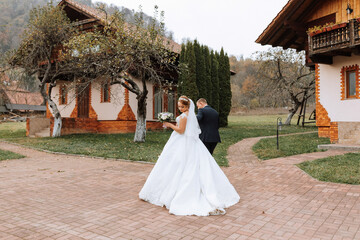 Fototapeta premium A bride and groom are walking down a path in front of a house. The bride is wearing a white dress and the groom is wearing a suit. The scene is peaceful and romantic, with the couple looking happy