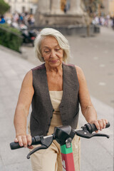 A woman dressed in a stylish yet casual outfit is having an enjoyable ride on her electric scooter in the city