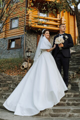 Fototapeta premium A bride and groom are standing on a set of stairs in front of a log cabin