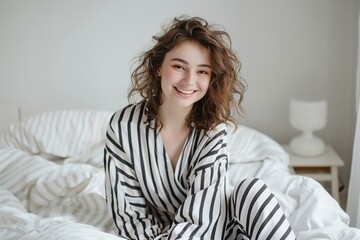 Naklejka premium Young happy girl in pajama sitting on bed after sleep