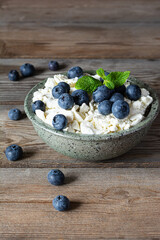 A bowl with cottage cheese, yogurt, fresh berries (blueberries) and fresh mint on a wooden background. Delicious breakfast, healthy food.