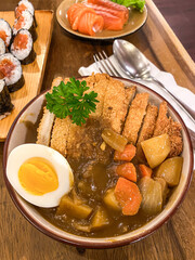 Japanese chicken katsu curry with boiled egg served in bowl on wooden table in a restaurant.