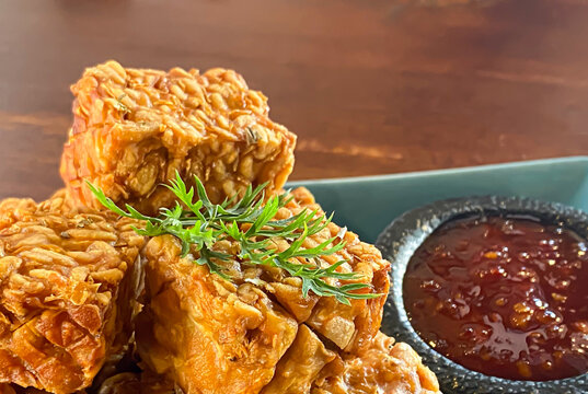 Pile of fried tempeh served on a blue squeare plate with chilli sauce sambal. Tempe is Indonesian traditional food contains high vegetable protein nutrition.