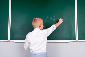 Photo of clever adorable boy standing in class room solve math task isolated on green board background