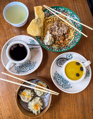 Fresh delicious breakfast with steamed shumai dimsum, noodles soup and butter coffee drinks on wooden table background. Vintage retro style kopitiam for breakfast.