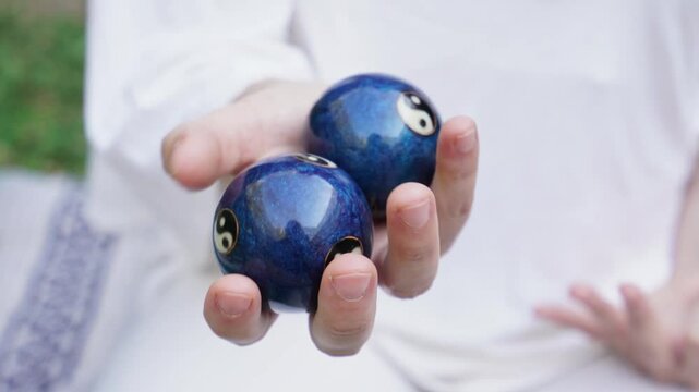 Two blue balls with yin and yang symbols on them. The person holding them is wearing a white shirt