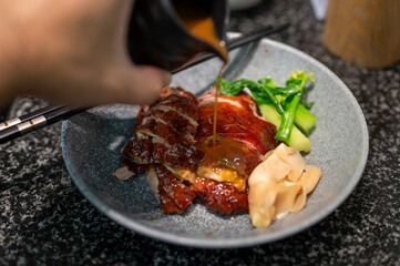 Roast duck in Chinese or Cantonese cuisine is served with a rich sauce, with green vegetables and pickled ginger on the side, making it a balanced and flavorful dish.
