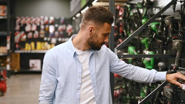 A man in a hardware store chooses a new screwdriver next to a showcase of power tools for repairs in the house.