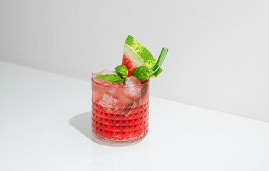 Glass of refreshing watermelon smoothie with basil, ice on white background with shadow.