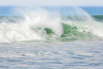 Fototapeta premium Huge ocean breaking wave sending up clouds of spray on a windy day