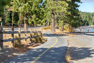 Empty winding bicycle lane running parallel to a road along the forested shoreline of a lake on a...