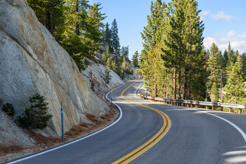 Empty winding mountain road line with pine trees under clear sky in autumn