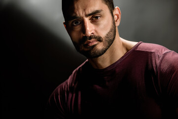 Fototapeta premium Portrait of strong handsome man with brutal unshaven face posing on dark background, Dark allure: Young man's serious gaze and beard create a powerful portrait against a gray background.