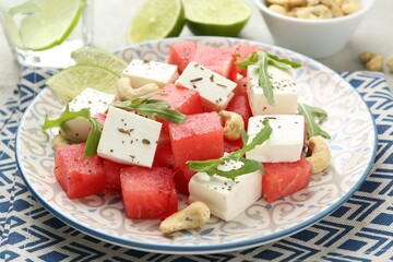 Delicious watermelon salad with feta cheese, cashew nuts and spices on light table, closeup