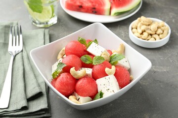 Delicious watermelon salad with feta cheese, cashew nuts and spices in bowl served on grey textured table