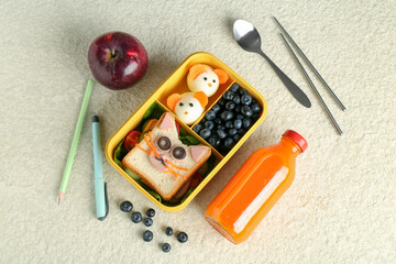 Lunch box with snacks, bottle of juice, cutlery, pen and pencil on beige textured table, flat lay