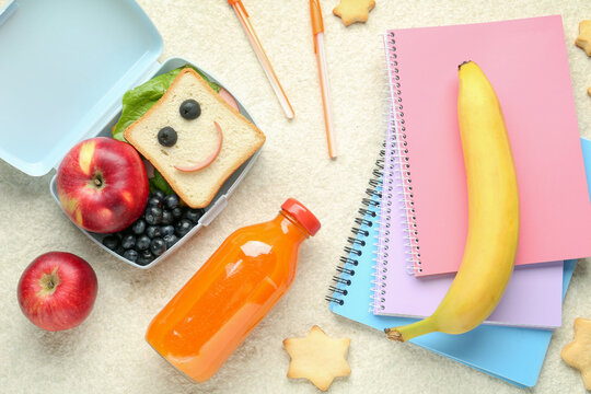 Lunch box with snacks, bottle of juice and stationery on beige textured table, flat lay