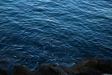 blue sea which looks calm and you can also see some somewhat dark rocks on the side