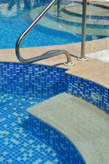 Swimming pool detail of tiles, steps and chrome handrail.