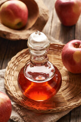 Apple cider vinegar in a glass bottle with ripe apples on a table