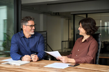 Two happy busy professional man and woman business leaders partners checking documents financial report project overview working together, manager consulting client in office at corporate meeting.