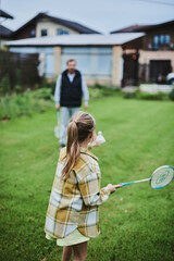 Teenage girl playing badminton with her father on green grass in summer park