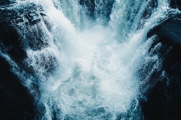 Aerial view of a powerful waterfall cascading into a deep pool, surrounded by rugged rock formations, showcasing nature's beauty.