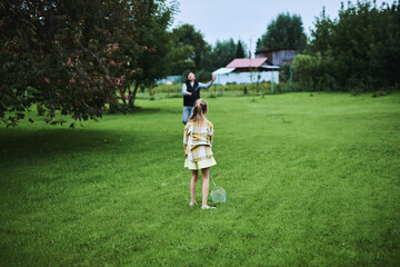 Teenage girl playing badminton with her father on green grass in summer park