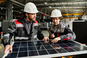 Engineers in hard hats examining solar panel in industrial environment, discussing installation process