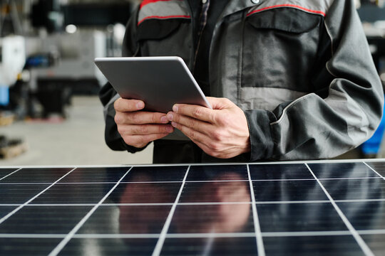 Worker examining solar panel with digital tablet in industrial workshop, suggesting modern technology integration and renewable energy focus