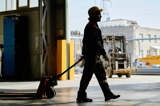 Construction worker holding pallet jack in spacious industrial warehouse with large windows