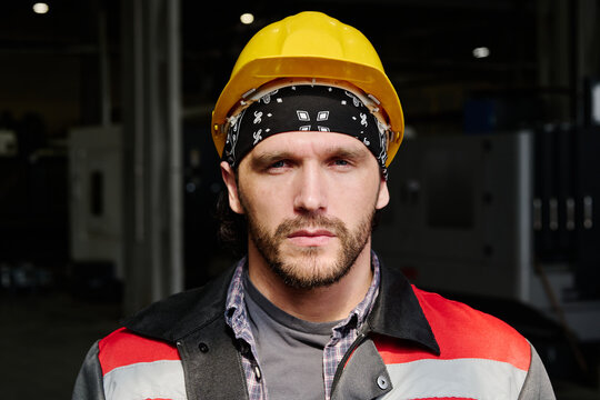 Portrait of construction worker wearing yellow helmet and bandana, standing in industrial setting 