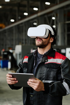 Man wearing VR headset and holding tablet in industrial setting examining advanced technology for manufacturing process improvement