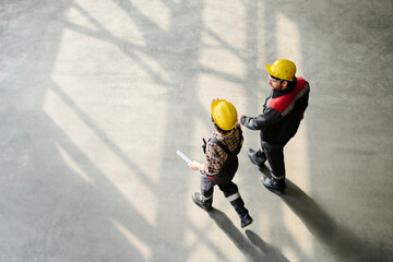 Two construction workers wearing protective gear and walking through the concrete site