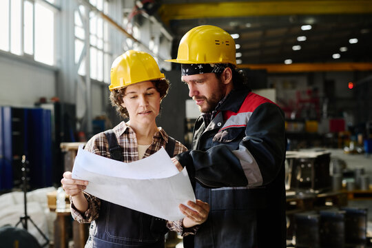 Two construction workers reviewing project blueprints inside large industrial facility