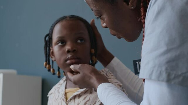 Close up shot of African American female physician asking little girl to show tongue and examining her throat at medical visit
