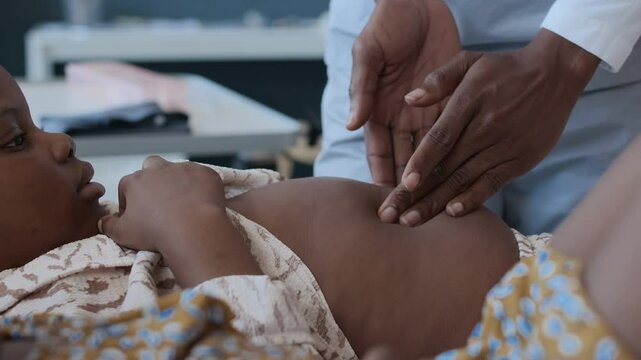 Close up view of hands of unrecognisable physician palpating abdomen of preschool girl lying on couch next to her sister at doctors office