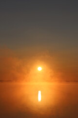 photo of a bright sunrise on a lake with haze