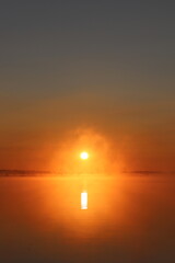 photo of a bright sunrise on a lake with haze
