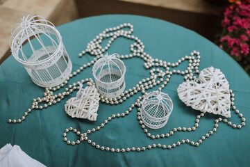 A table with a blue cloth and a white bird cage with a heart on it. There are also other white bird...