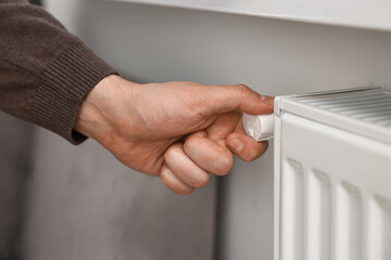 Man adjusting temperature of heating radiator indoors, closeup