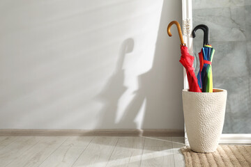 Bright umbrellas in holder and mirror near white wall. Space for text © New Africa