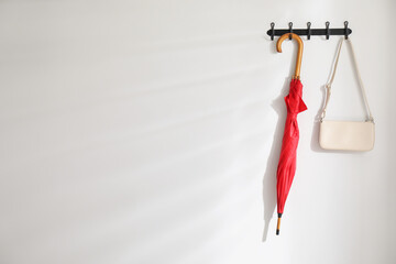 Red umbrella and bag on hanger near white wall. Space for text