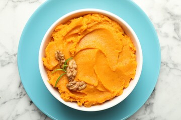 Delicious mashed sweet potatoes with walnuts in bowl on white marble table, top view