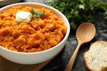 Delicious mashed sweet potatoes with butter, parsley, bread and spoon on dark table, closeup