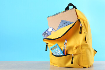 Naklejka premium Backpack with different school stationery on wooden table against light blue background, space for text