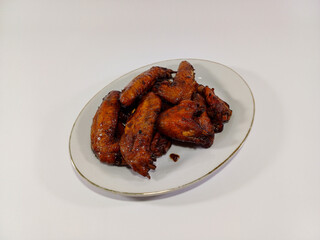 Indonesian Chicken Wings in Sweet Soy Sauce with a Drizzle of Honey: Flavorful and Succulent Wings Served on a White Oval Plate Against a White Background, Perfectly Balancing Sweet and Savory Tastes