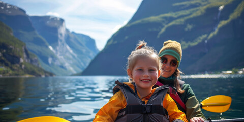 A girl and her mother in a boat are sailing along a sea bay with mountains in the background.