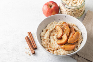 Sweet oatmeal porridge with baked apple slices, cinnamon and caramel sauce in a gray bowl on a light background